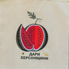 A beige canvas tote bag with a embroidered watermelon graphic and Cyrillic text, hanging against a dark brown woven bamboo background.