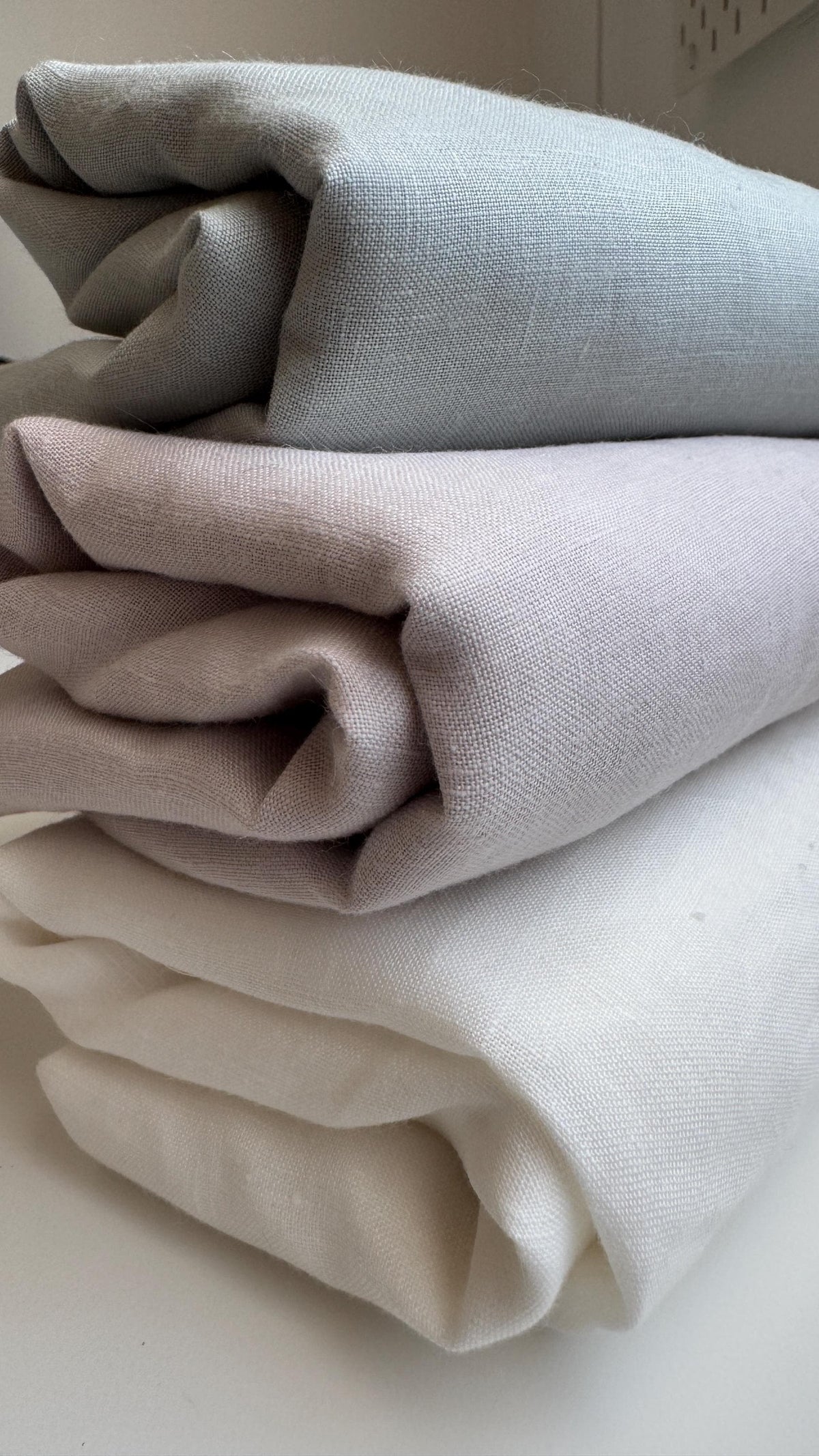 Three folded pieces of textured fabric in light gray, dusty pink, and cream white, stacked on a light surface.