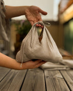 Hands holding a small natural linen bento bag with ties