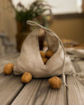 Linen bread bag with corner ties filled with walnuts on a wooden table