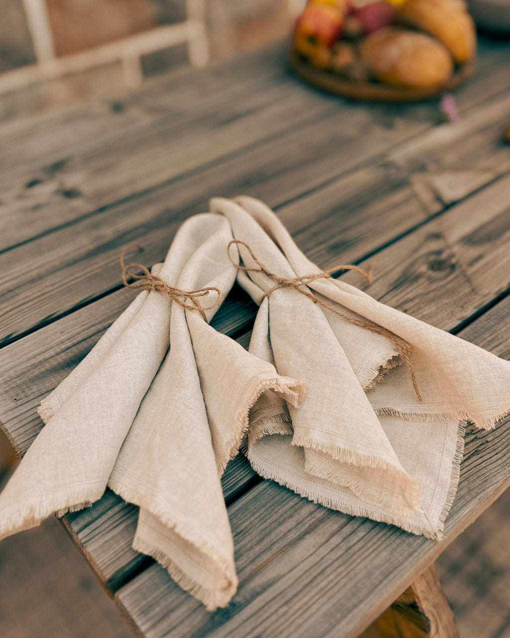 Two folded natural linen napkins tied with twine, displayed on a rustic wooden table.