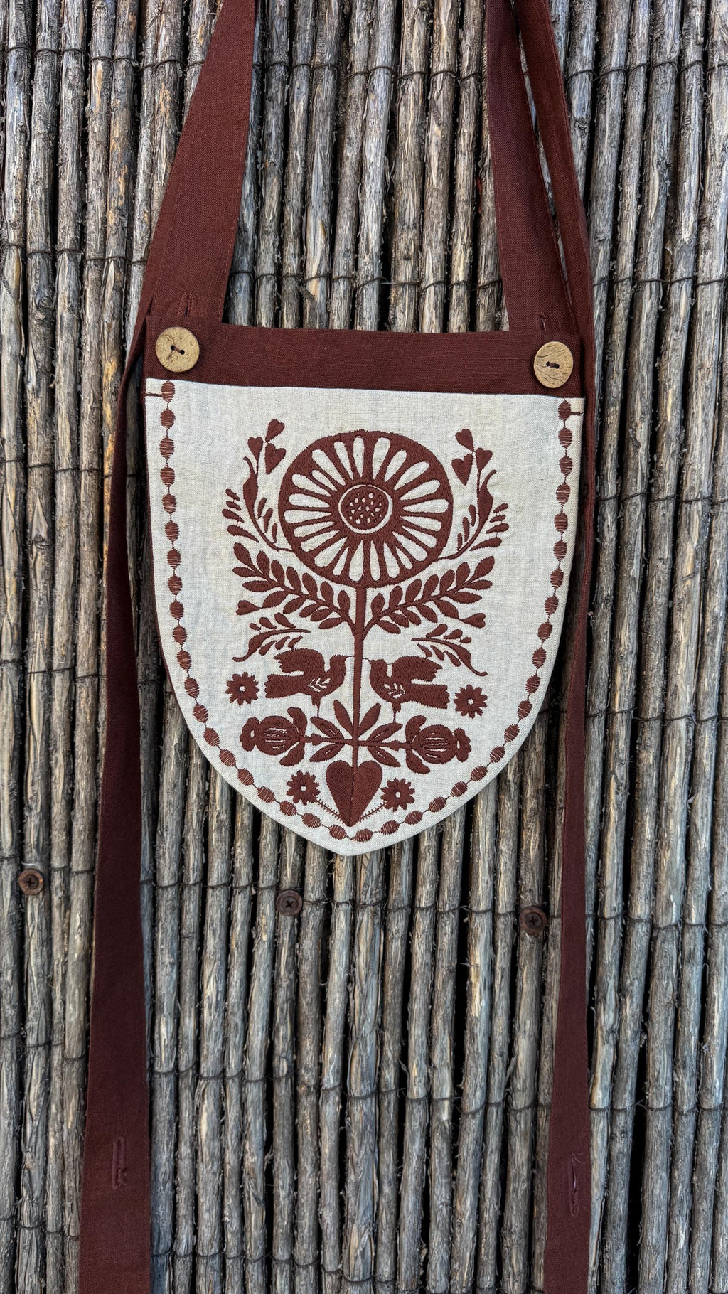 Linen belt bag with a long chocolate strap against a reed fence