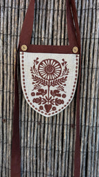Linen belt bag with a long chocolate strap against a reed fence