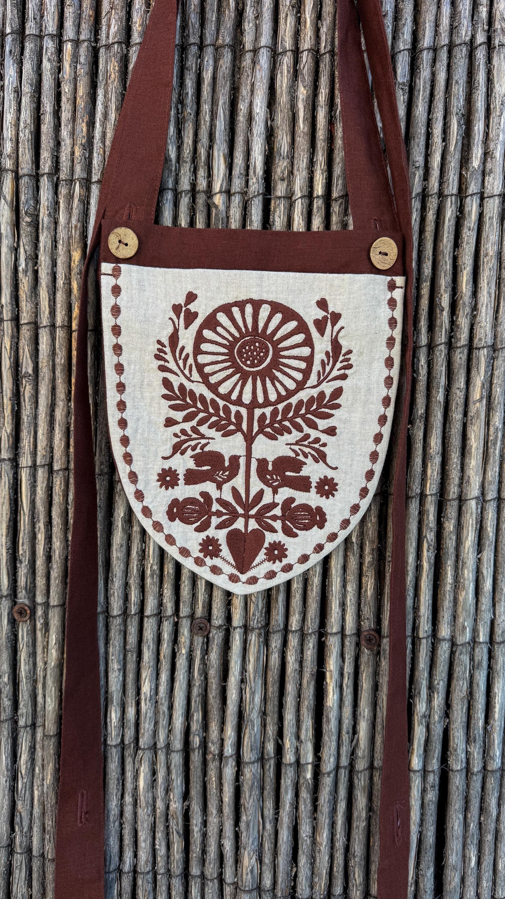 Linen belt bag with a long chocolate strap against a reed fence
