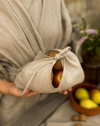 Linen bento bag holding fruit, carried by its ties, with lemons and walnuts behind