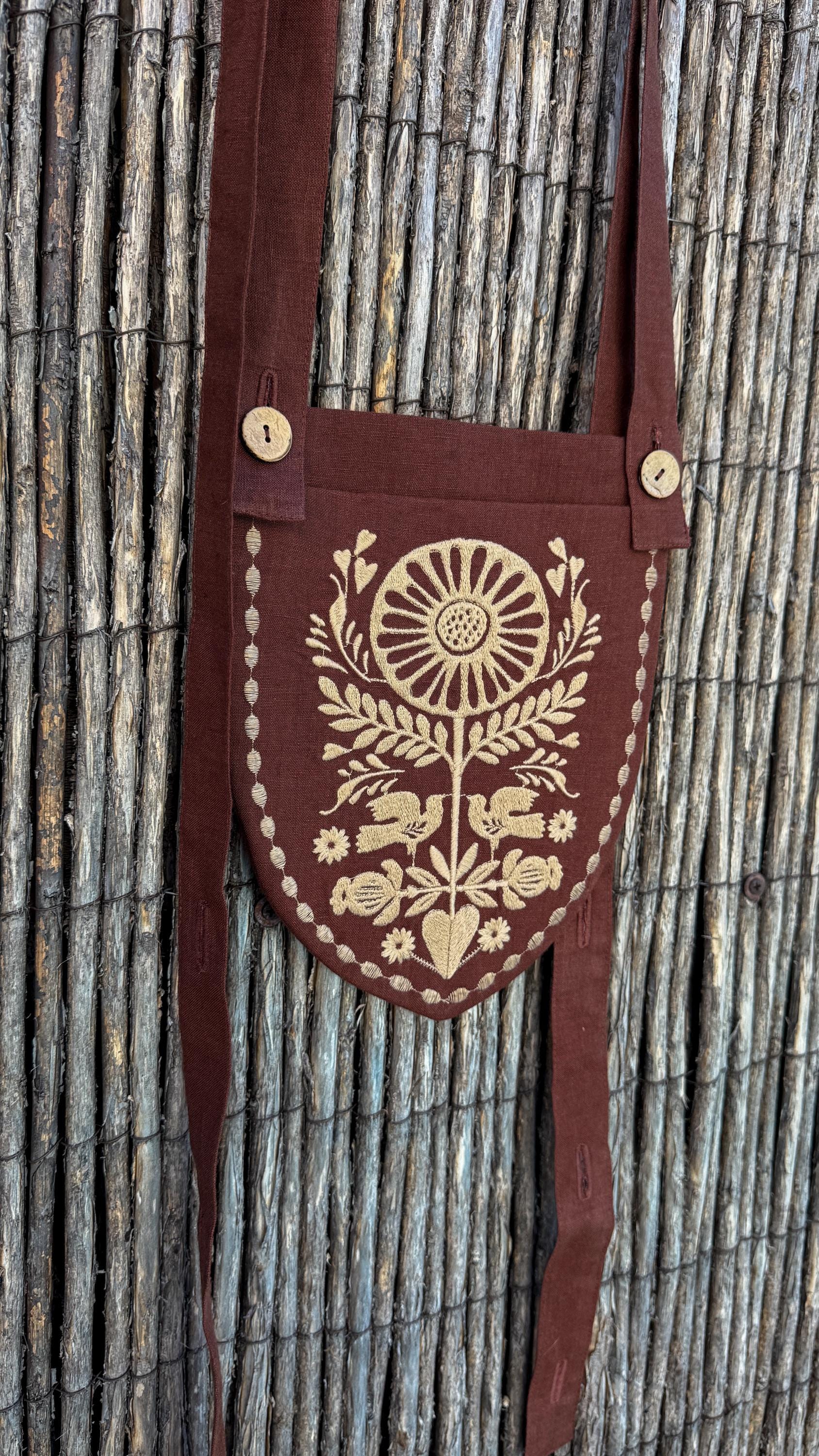 Brown belt pouch with its long strap against a reed fence