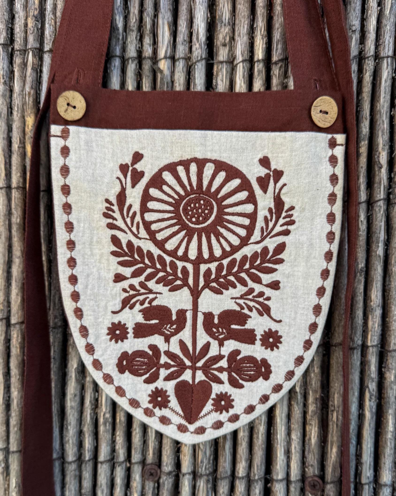 Linen belt bag with chocolate embroidery hanging on a reed fence
