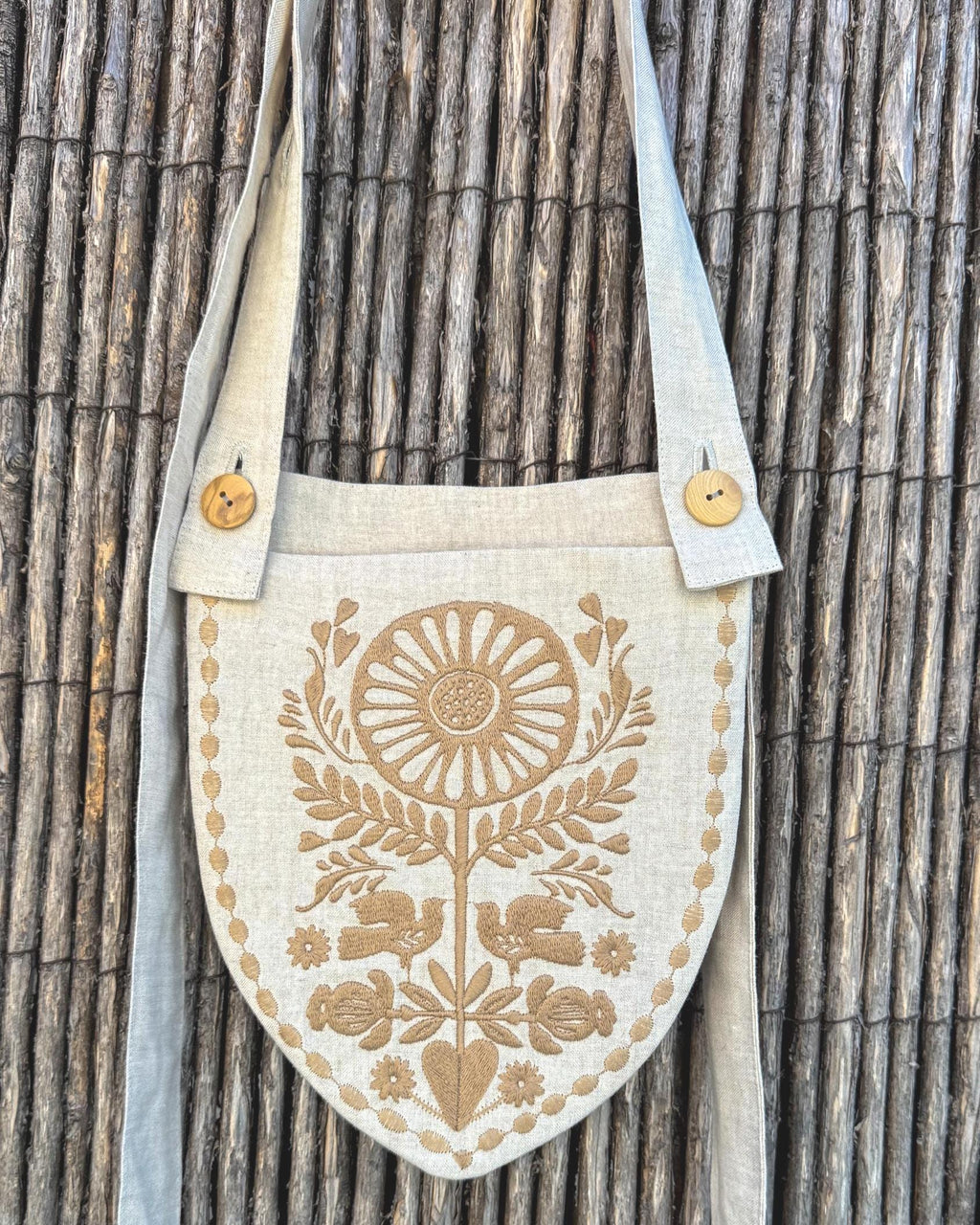 Linen belt bag with sand embroidery hanging on a reed fence