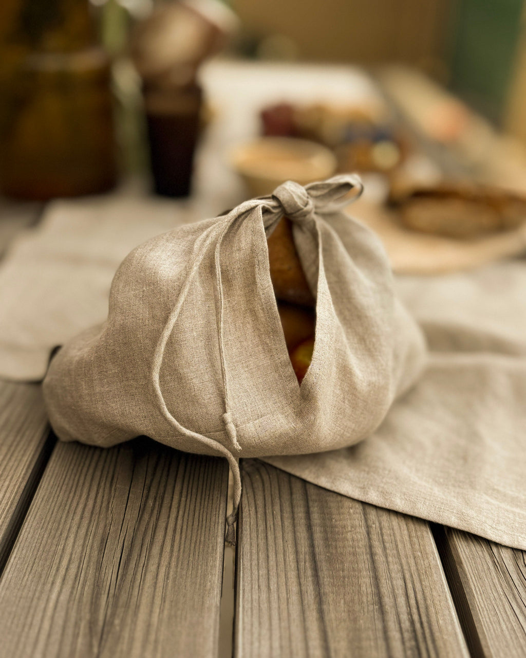 Linen bread bag holding a loaf of bread on a rustic wooden table