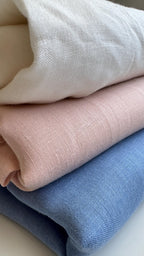 Three folded textured fabrics stacked diagonally, showing off-white, dusty pink, and light blue colors.