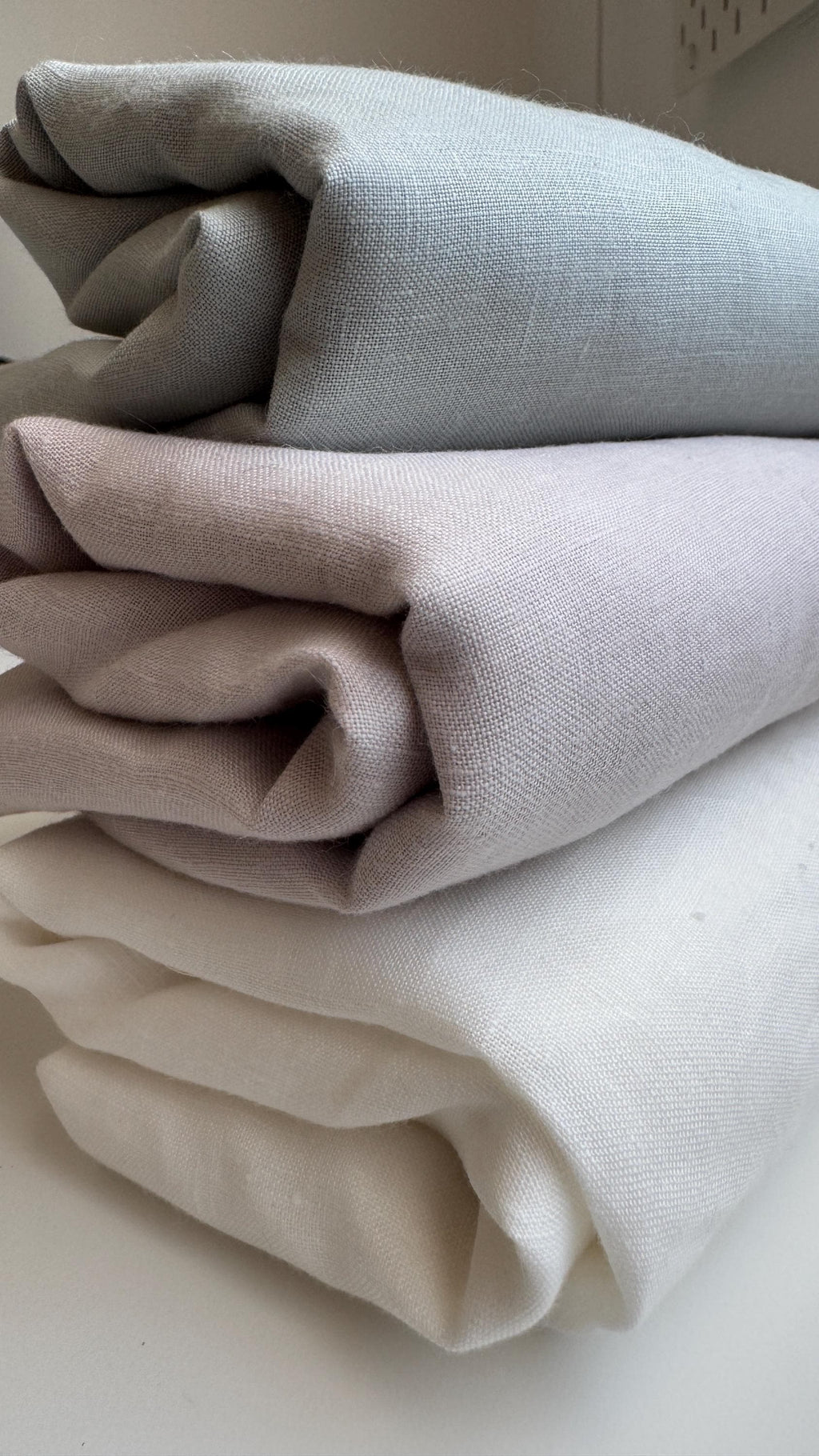 Three folded pieces of textured fabric in light gray, dusty pink, and cream white, stacked on a light surface.