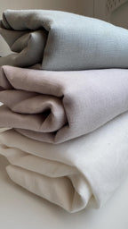 Three folded pieces of textured fabric in light gray, dusty pink, and cream white, stacked on a light surface.