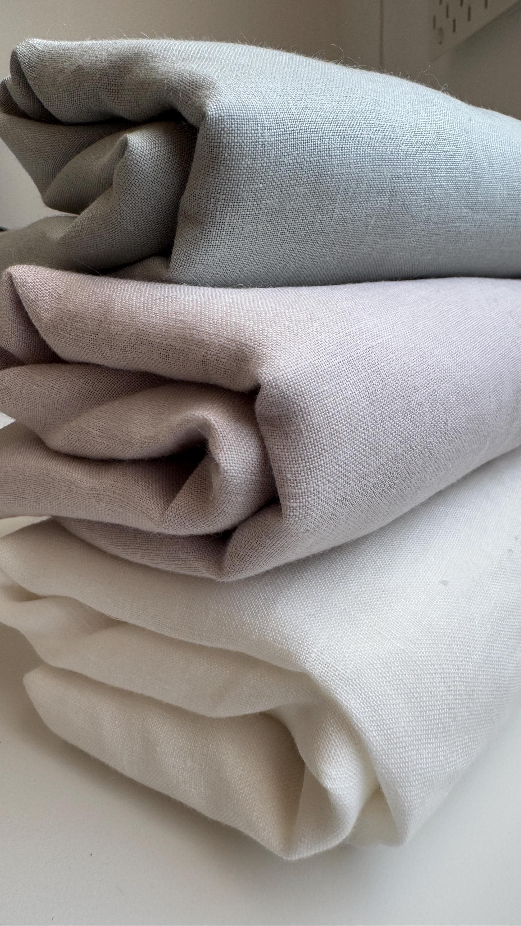 Three folded pieces of textured fabric in light gray, dusty pink, and cream white, stacked on a light surface.
