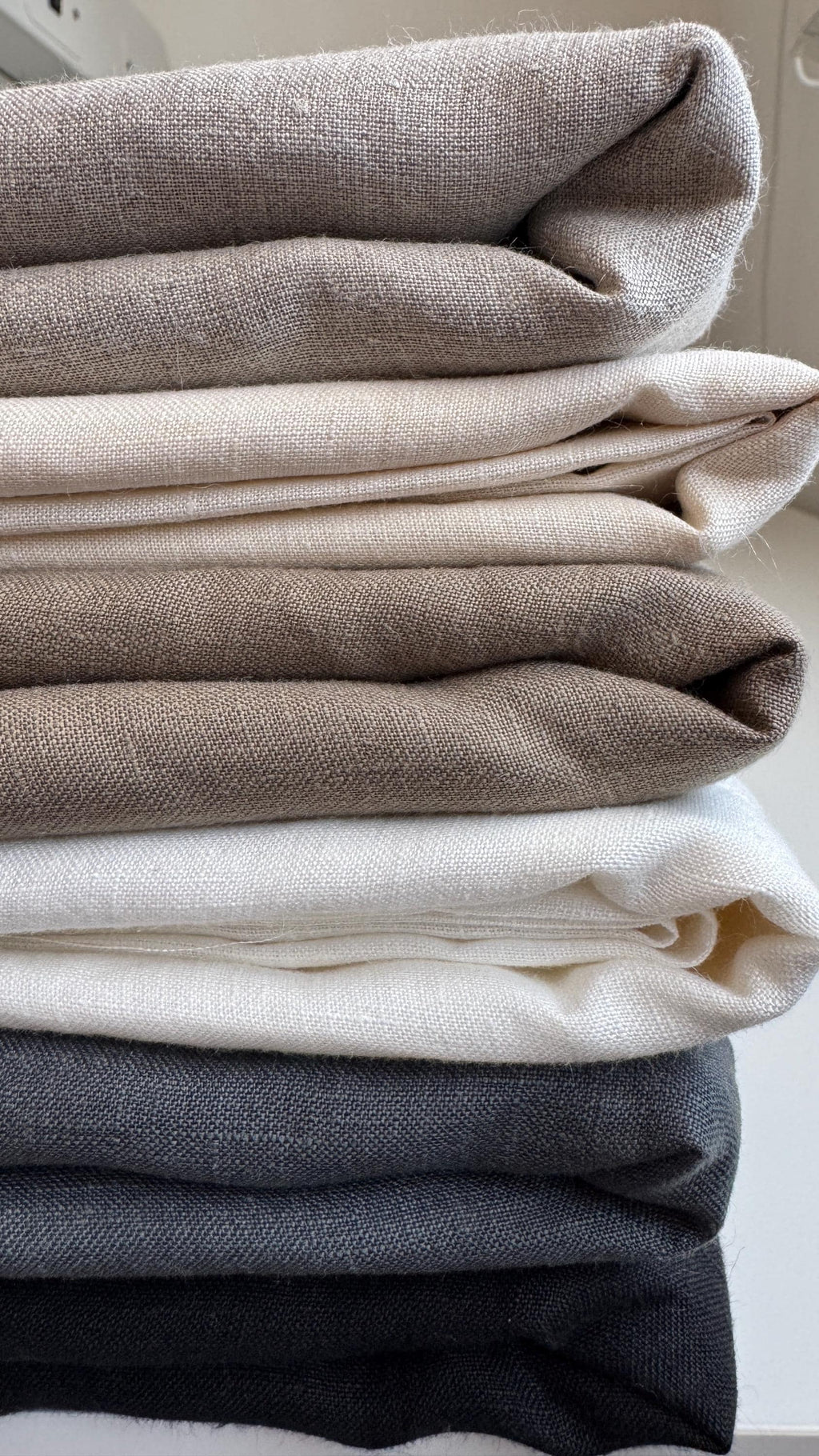 Stack of folded linen squares in cream, grey and charcoal