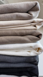 Stack of folded linen squares in cream, grey and charcoal