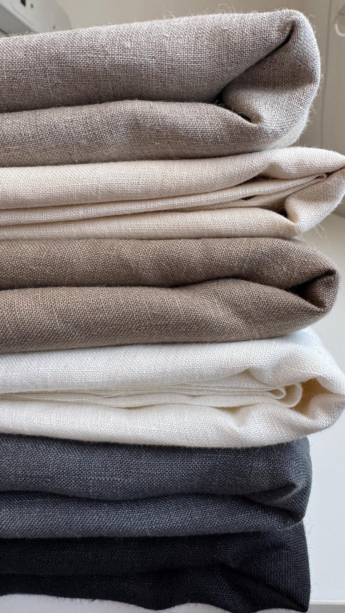 Stack of folded linen squares in cream, grey and charcoal