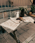 Embroidered linen table runner in natural Belgian linen with wheat design, set on a wooden table with bread and fruit