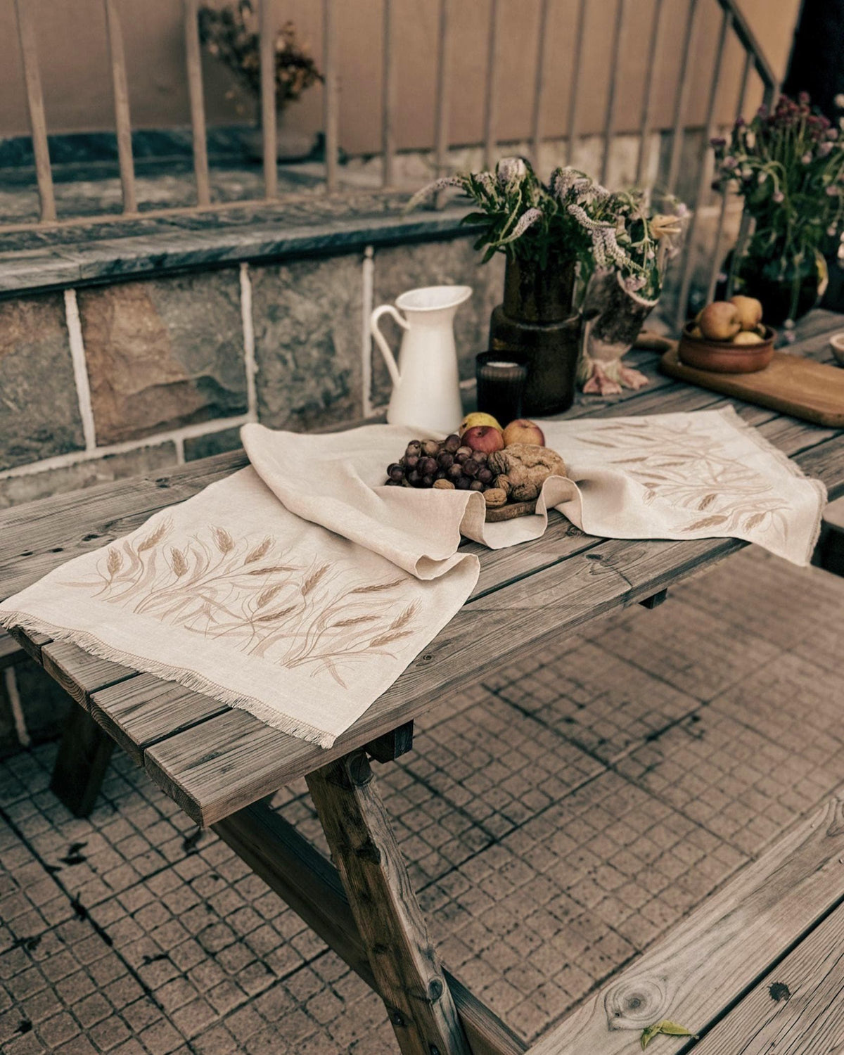 Embroidered linen table runner in natural Belgian linen with wheat design, set on a wooden table with bread and fruit