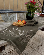 An embroidered linen table runner in natural Belgian linen — wheat ears stitched in warm wheat-coloured thread across both ends. 